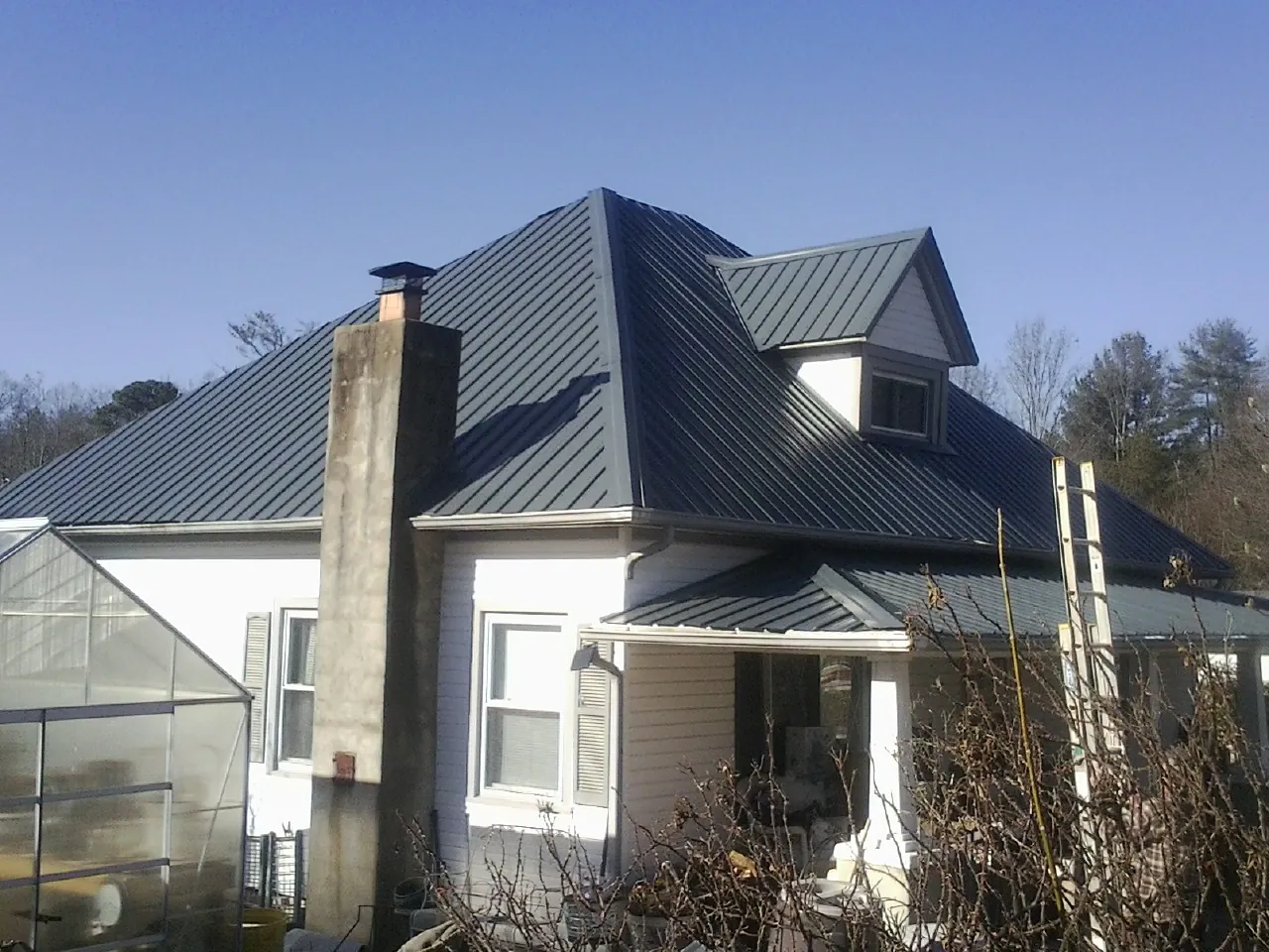 Dark blue standing seam metal roof on a white farmhouse with dormer — Slate & Tile Roof Repair by Roofing Brothers in Green Village