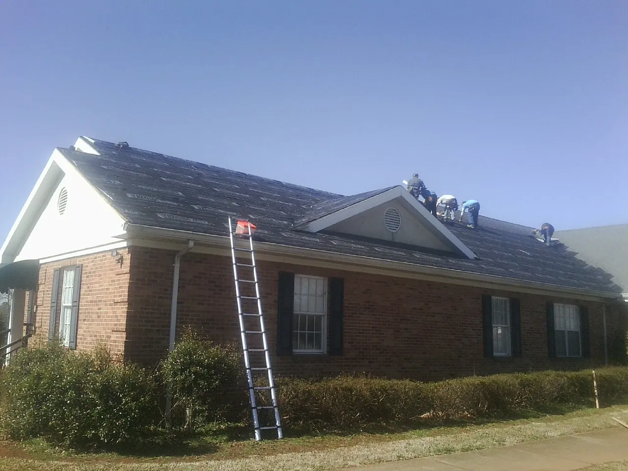 Crew tearing shingles off a brick ranch roof with a ladder set — Emergency Roof Repair work by our crew in Green Village