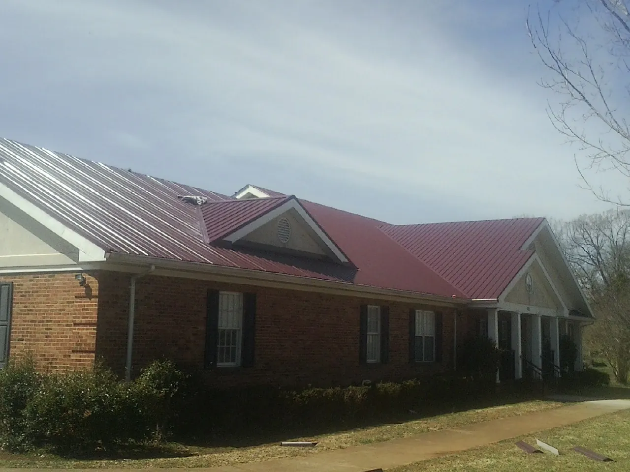 Red metal roof with gabled entries on a long brick building, from a Hail Damage Roof Repair job in Green Village