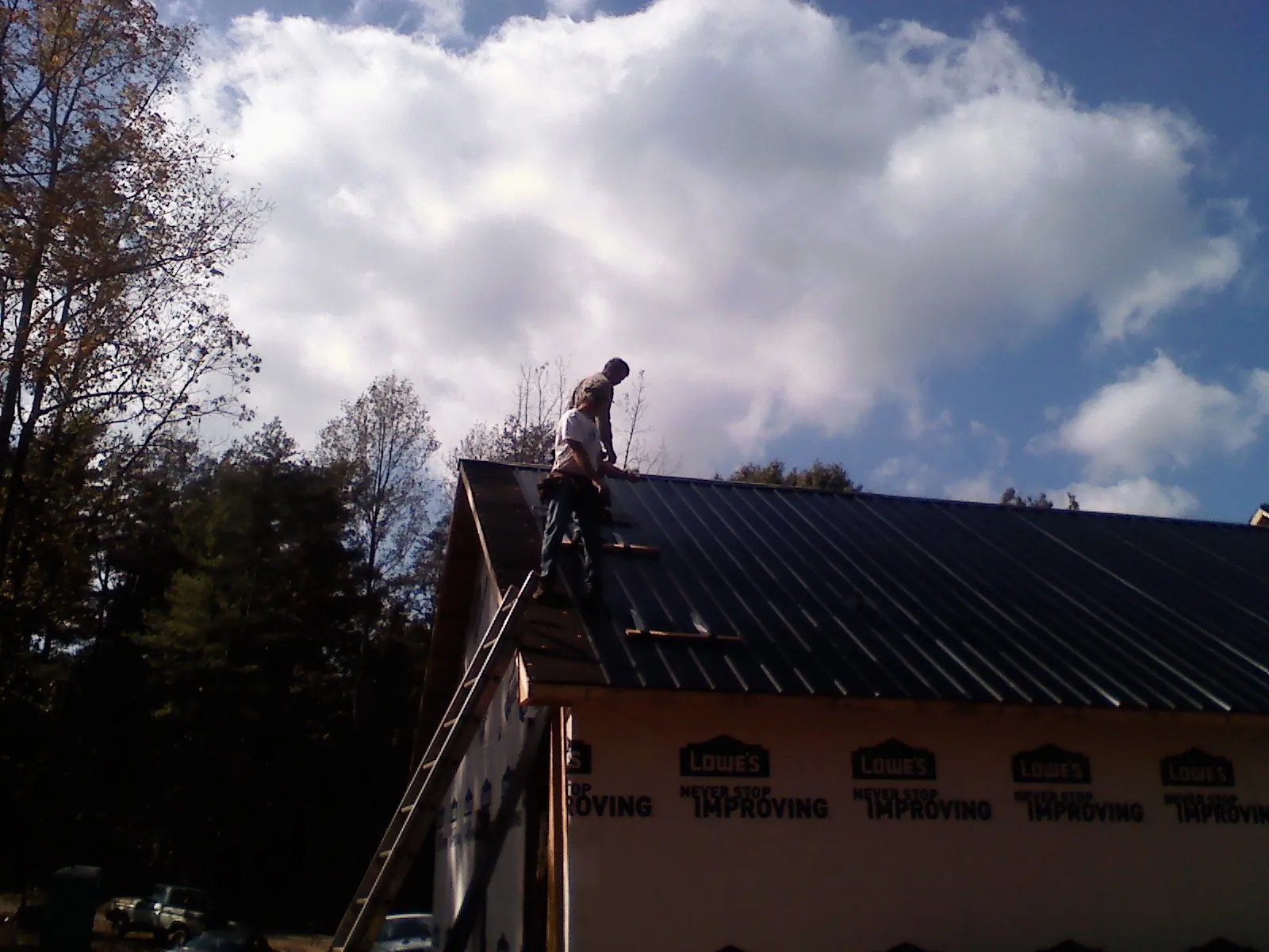 Roofer fastening dark metal panels high against a cloudy sky, from a Roof Inspection job in Green Village