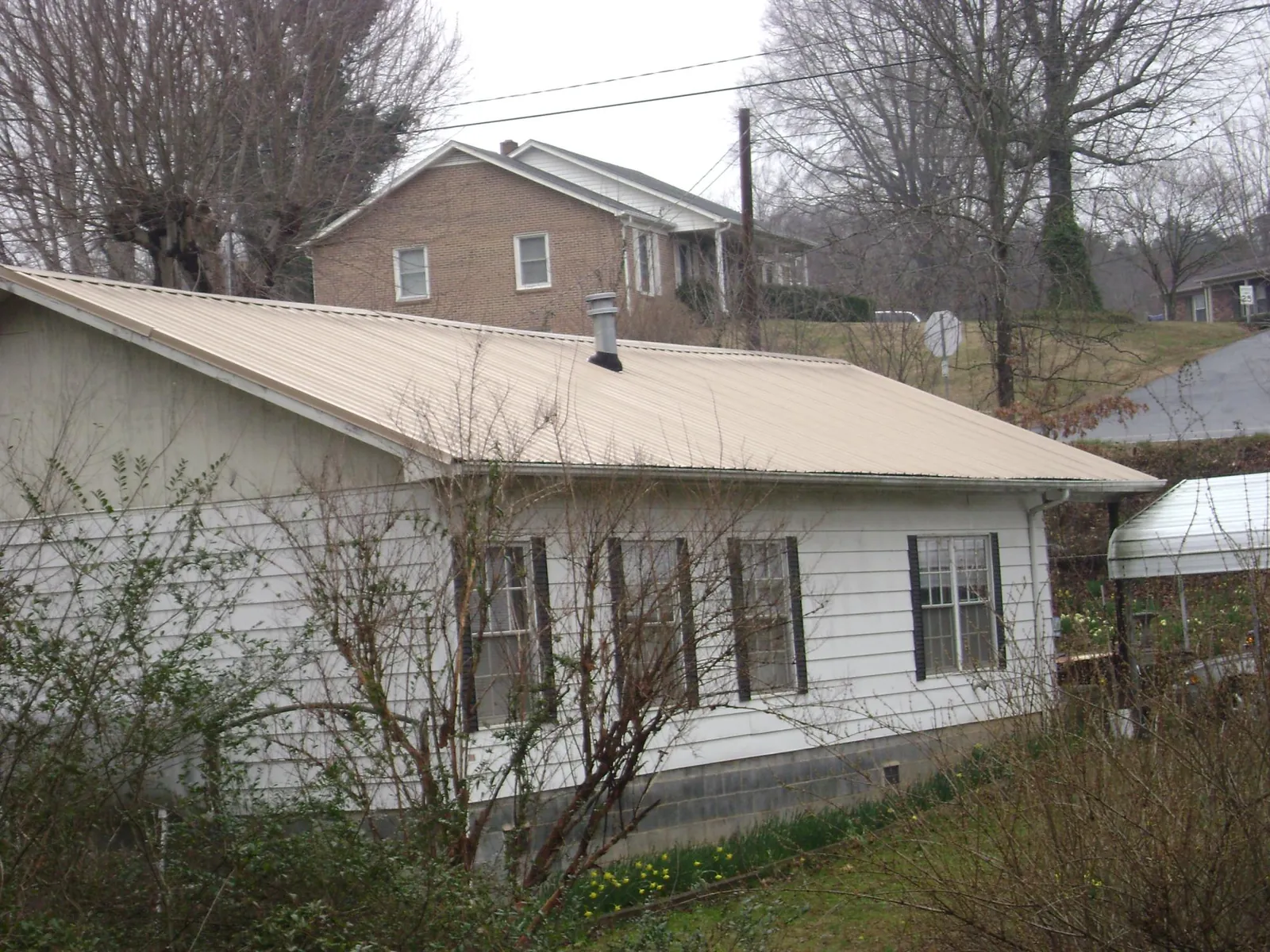 Tan metal roof on a white sided house set into a hillside — Commercial Roofing by Roofing Brothers in Green Village